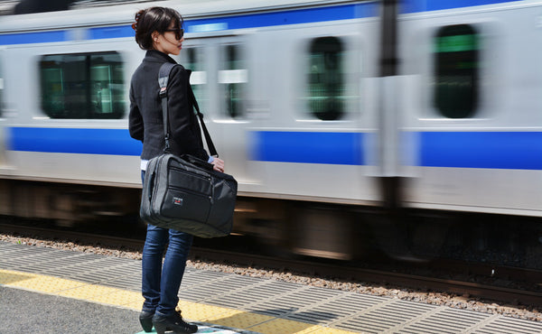 A person carrying a Black 525 Ballistic Western Flyer using the included backpack straps as a rail car passes by.